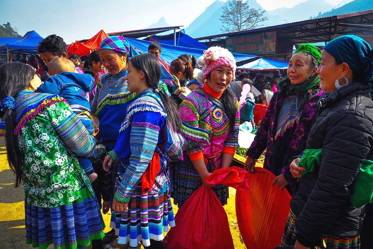 Can Cau Market Lao Cai women chatting in ethnic dress Ethnic women in vibrant traditional dress chat and smile at Can Cau Market in Lao Cai