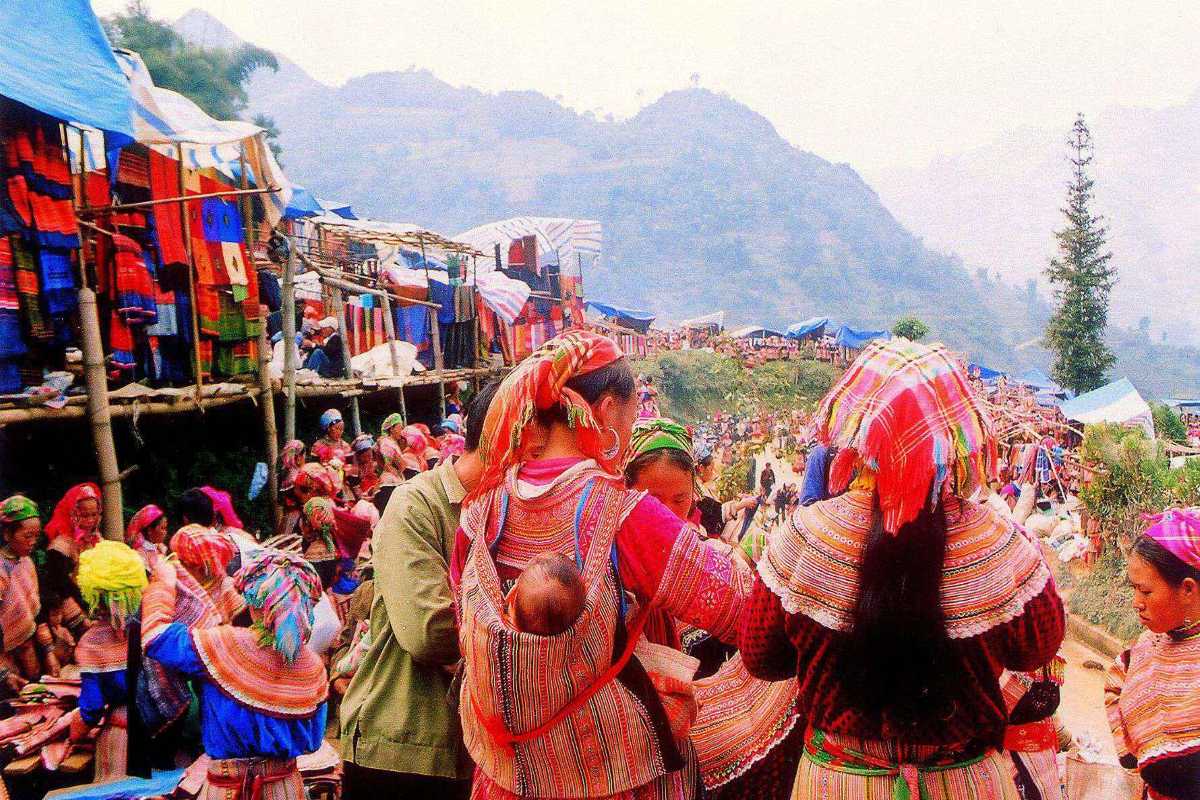Can Cau Market Lao Cai hillside bazaar view with shoppers Brightly dressed shoppers browse fabric and goods along hillside stalls at Can Cau Market in Lao Cai