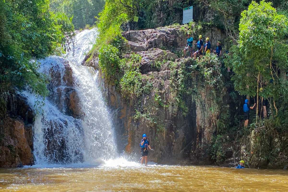 Canyoning Adventure at the Base of Datanla Waterfalls Group preparing for canyoning at the rocky base of Datanla Waterfalls surrounded by tropical greenery