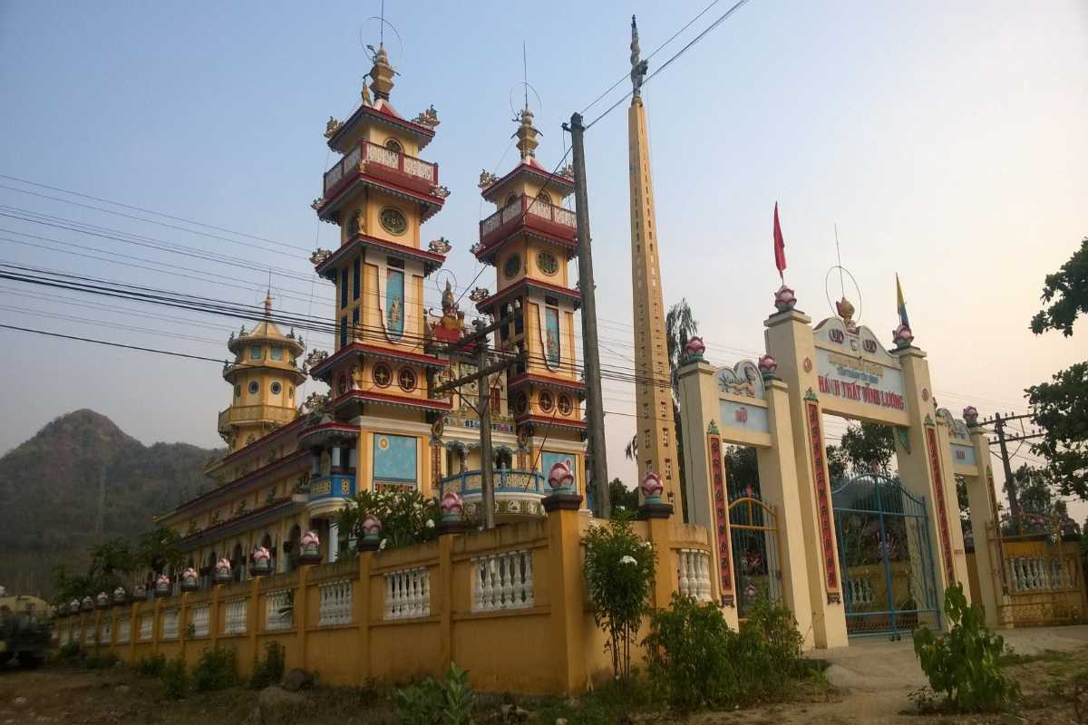 Cao Dai Temple in Vĩnh Lương Colorful Cao Dai temple facade with towers and banners near a mountain backdrop in Vĩnh Lương.
