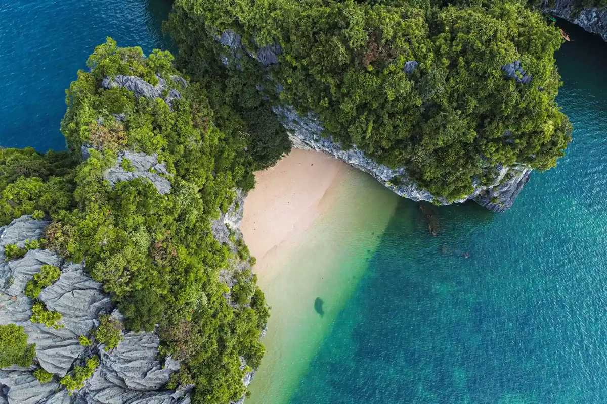 Cap La Island Bai Tu Long Bay aerial beach view Aerial view of Cap La Island in Bai Tu Long Bay showing pristine beach, turquoise water, and limestone cliffs
