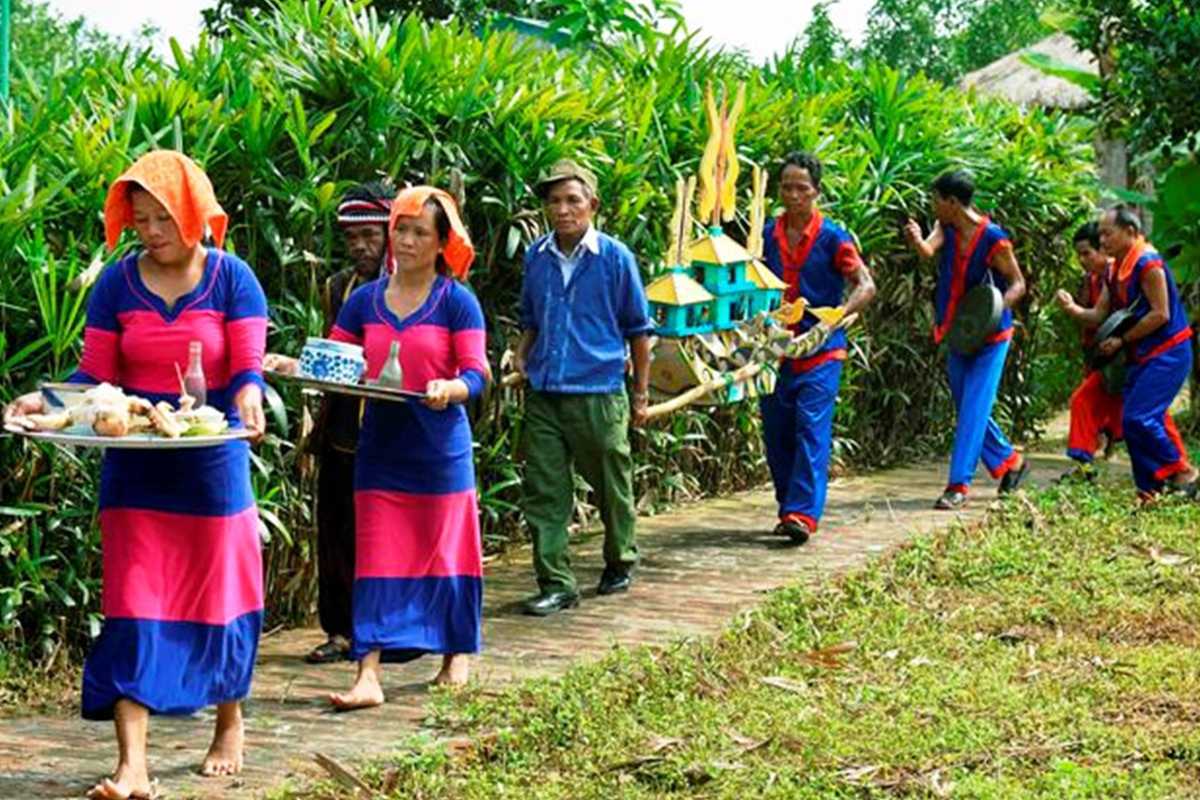 Cham women during ritual offering Cham women in pink and blue dresses carry ceremonial offerings through a village path near the Cai River.