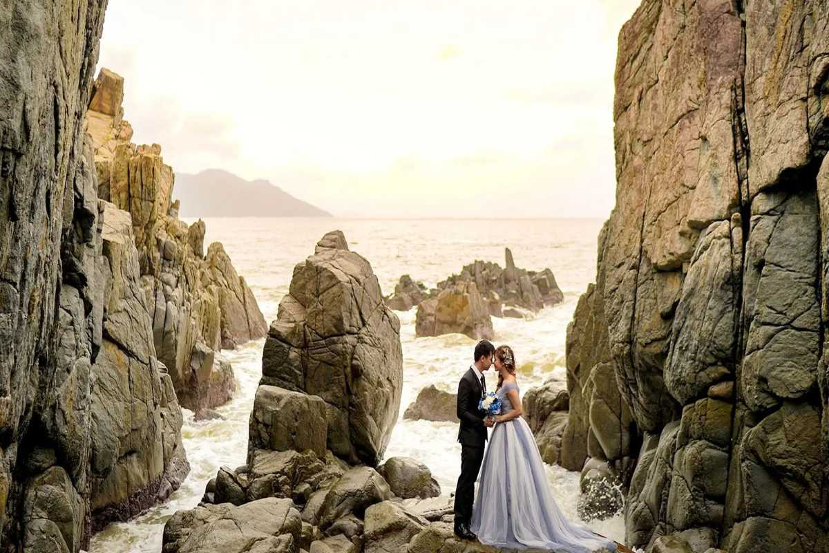 Couple at Cliffside in Vĩnh Lương A bride and groom pose between dramatic sea cliffs with waves crashing below in Vĩnh Lương.