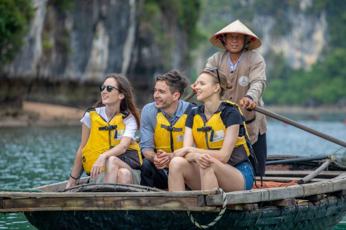 Close-Up Bamboo Boat Experience in Ba Hang Smiling tourists in life jackets ride a bamboo boat steered by a local rower in Ba Hang Fishing Village, Halong Bay.