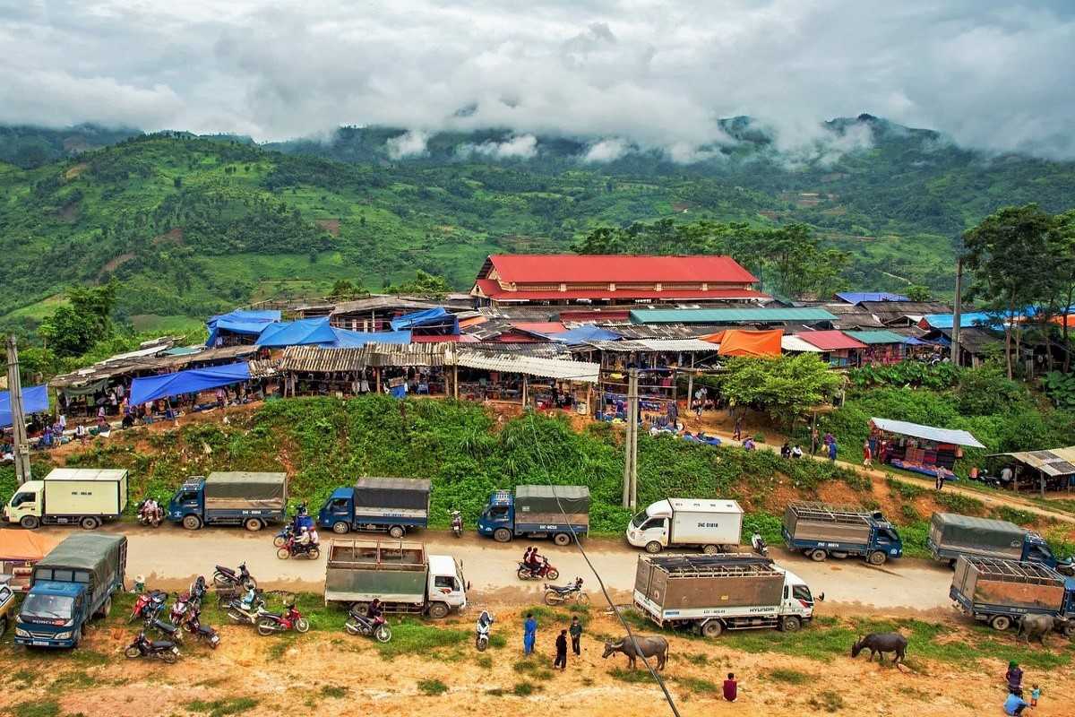 Coc Ly Market overview with blue tarps and hills Aerial view of Coc Ly Market with colorful canopies and trucks parked along the roadside in Lao Cai's highlands.