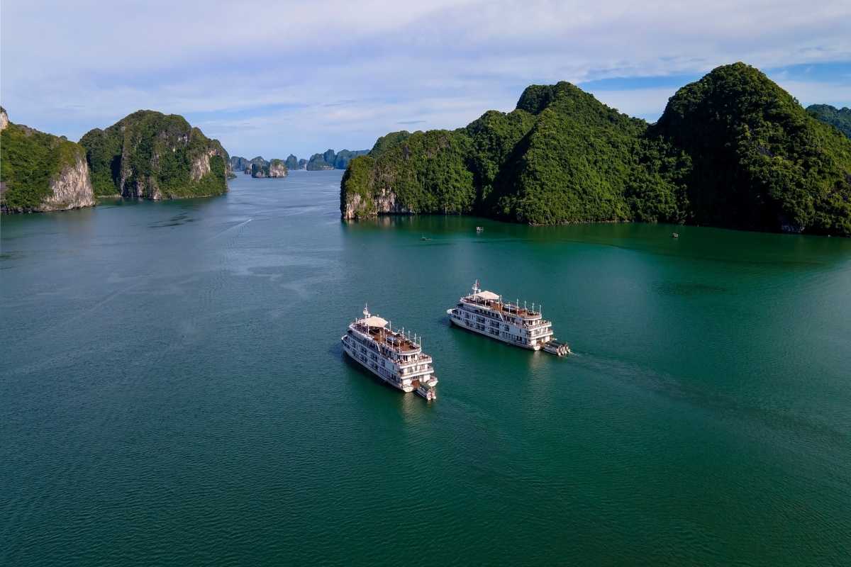 Cong Do Island Bai Tu Long Bay luxury cruise ships in emerald bay Two luxury cruise ships sailing in the emerald waters of Cong Do Island Bai Tu Long Bay, surrounded by green cliffs.