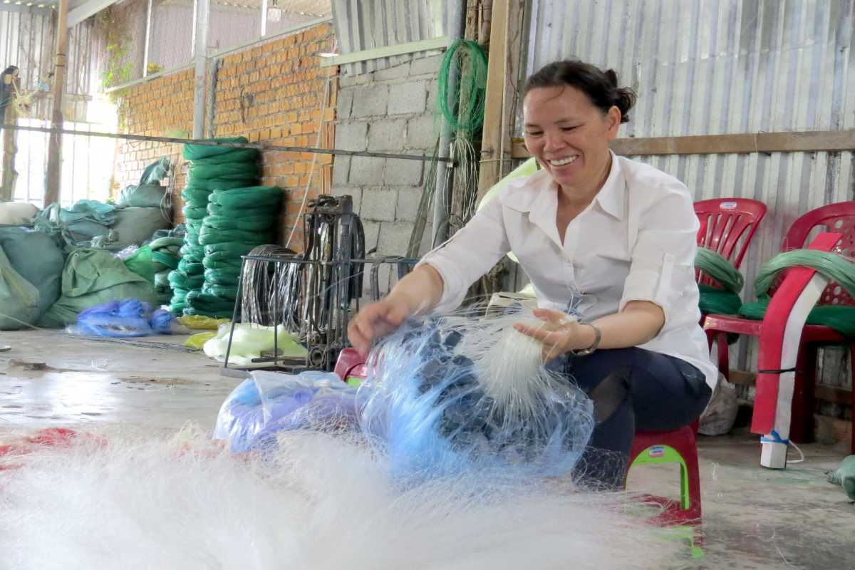 Handcrafting Nets at Cai River Village A smiling woman hand-spinning fishing nets in a riverside craft village near Cai River in Nha Trang.