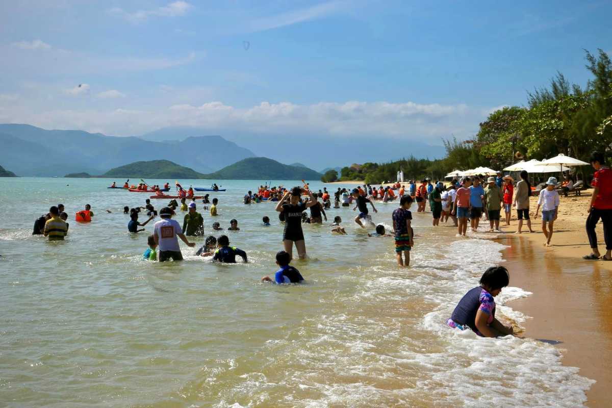 Crowded Beach at Orchid Stream Island Nha Trang Visitors swimming and playing on the beach with forested hills in the background at Orchid Stream Island