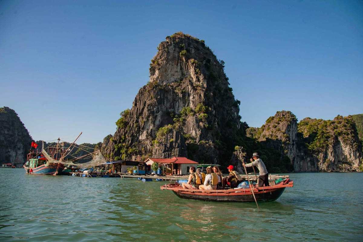 Cua Van Floating Village Halong Bay traditional fishing boat Traditional fishing boat moored next to colorful floating houses in Cua Van Floating Village Halong Bay with lush cliffs behind