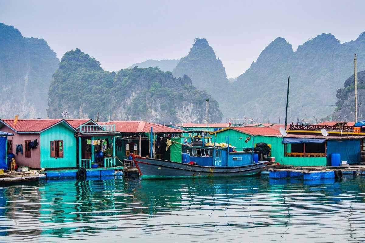 Cua Van Floating Village Halong Bay Panorama Panoramic view of Cua Van Floating Village with boats, homes, and limestone karsts under a cloudy sky
