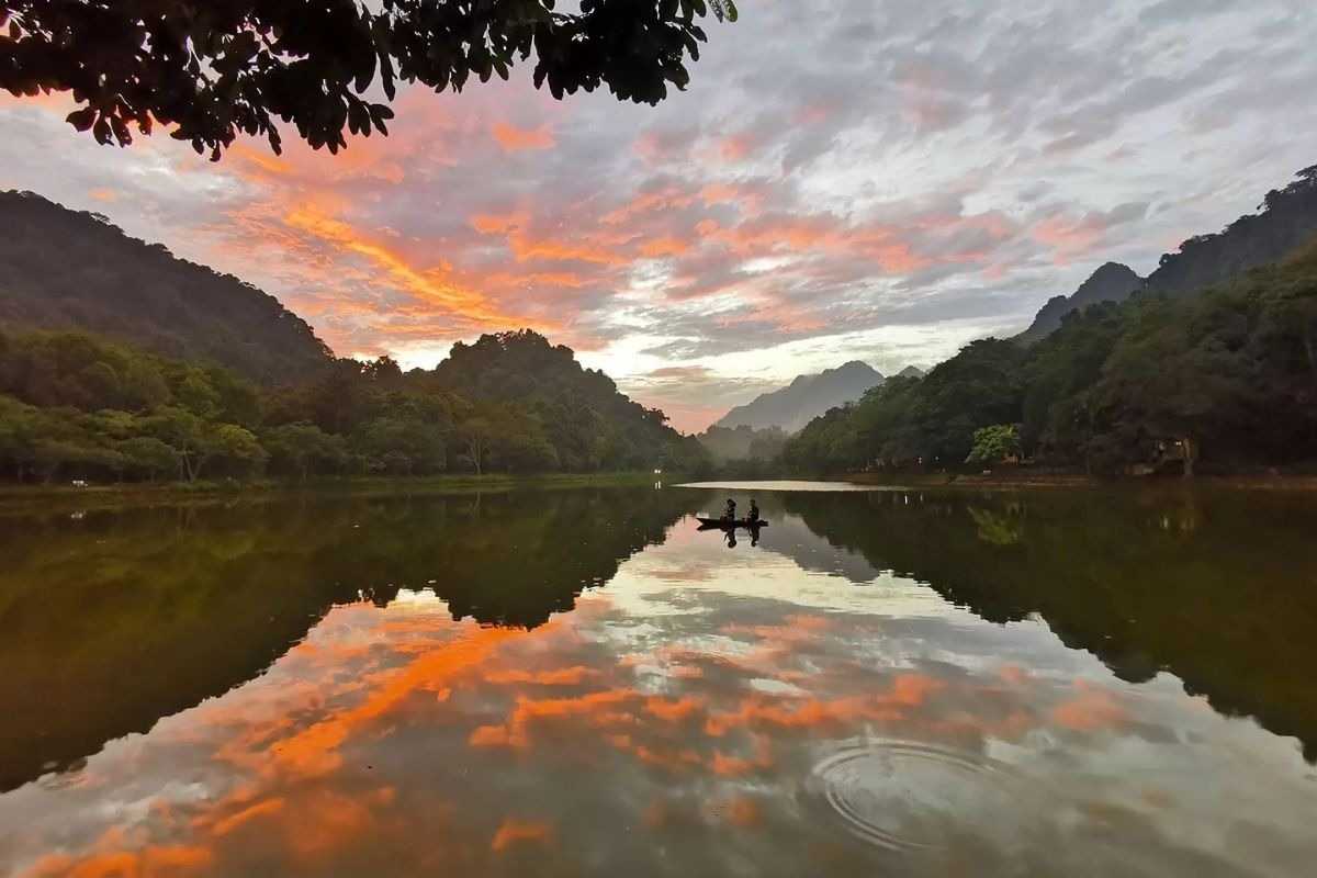 Cuc Phuong National Park scenic lake sunset reflection view A scenic lake in Cuc Phuong National Park Ninh Binh reflects a colorful sunset sky and surrounding hills.