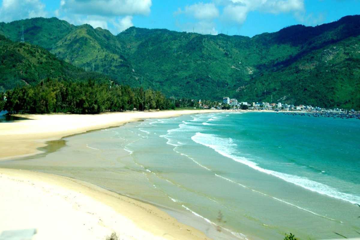 Pristine sandy shoreline of Dai Lanh Beach with lush green mountains in the background under a partly cloudy sky