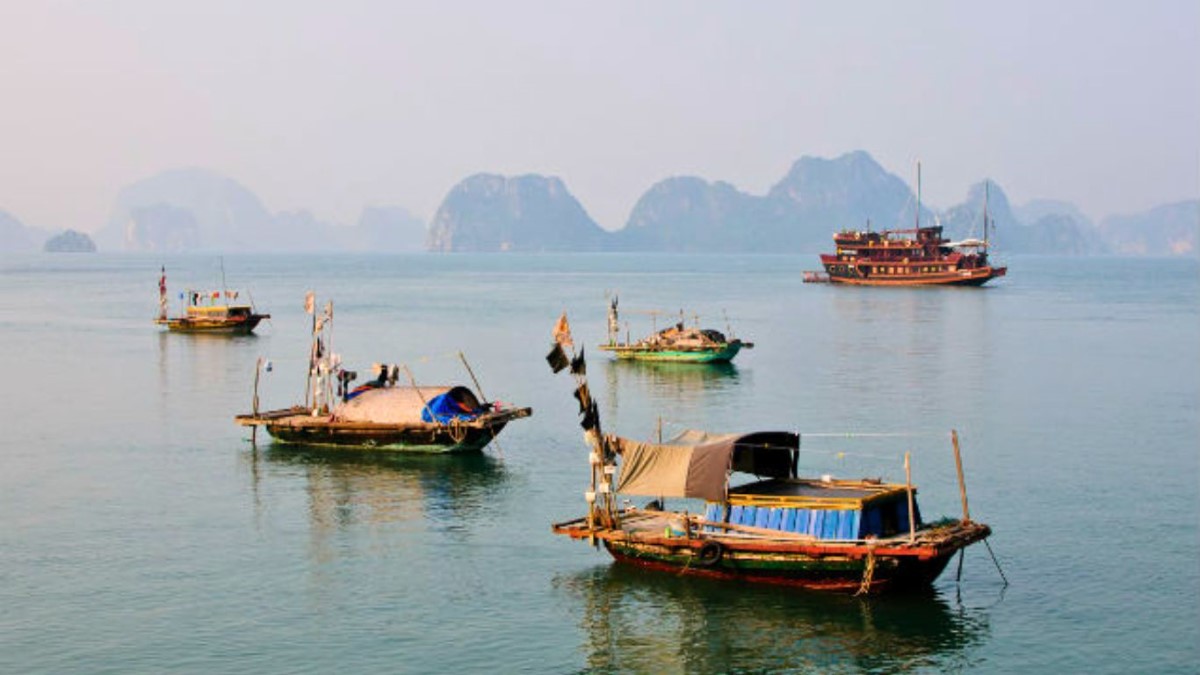 Daily life in Vung Vieng Fishing Village, featuring local boats and floating homes against a backdrop of limestone karsts in Bai Tu Long Bay.