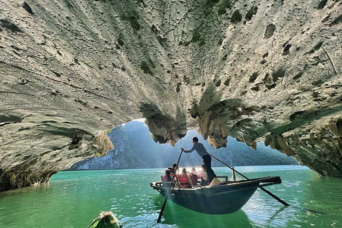 Dark and Bright Cave Halong Bay arched ceiling reflections A rowboat glides beneath the arched limestone ceiling of Dark and Bright Cave Halong Bay, with reflections on green water.