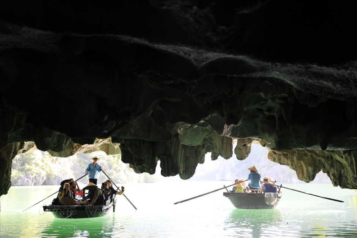 Dark and Bright Cave Halong Bay bamboo boat tour entrance Bamboo rowboats with visitors entering Dark and Bright Cave Halong Bay, sunlight filtering through cave mouth