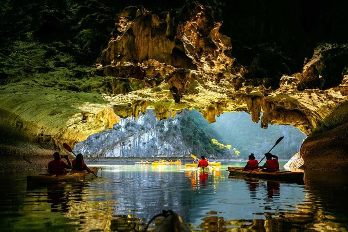 Dark and Bright Cave Halong Bay golden light kayaking adventure Kayakers paddling through Dark and Bright Cave Halong Bay illuminated by golden light inside the tunnel