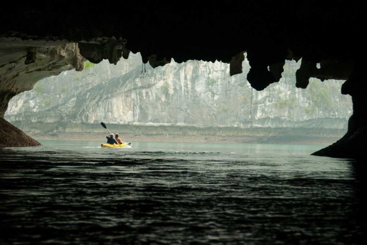 Dark and Bright Cave Halong Bay kayak lagoon view View from inside Dark and Bright Cave Halong Bay showing kayakers and dramatic limestone cliffs across the lagoon