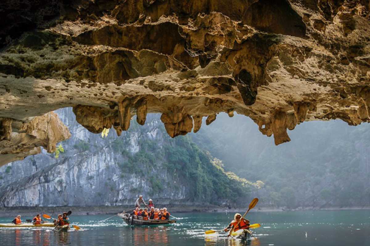 Dark and Bright Cave Halong Bay kayaking and rowboats Kayakers and rowboats gather inside the dramatic ceiling of Dark and Bright Cave Halong Bay, illuminated by soft sunlight.