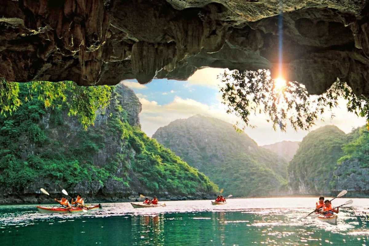 Dark and Bright Cave Halong Bay kayaking sunlit exit Kayakers paddle from the shadowy interior of Dark and Bright Cave Halong Bay toward a sunlit exit framed by limestone.