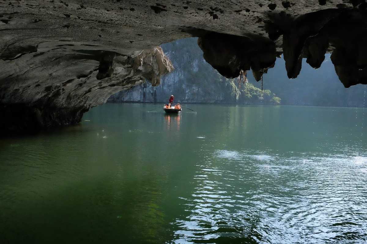Dark and Bright Cave Halong Bay peaceful rowboat lagoon Local rowboat floating in a calm, secluded lagoon inside Dark and Bright Cave Halong Bay, surrounded by cliffs