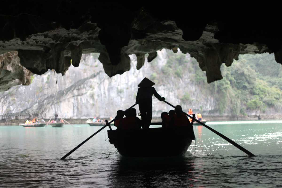 Dark and Bright Cave Halong Bay rowboat silhouettes A rowboat silhouette, framed by stalactites, emerges from the darkness of Dark and Bright Cave Halong Bay into daylight.