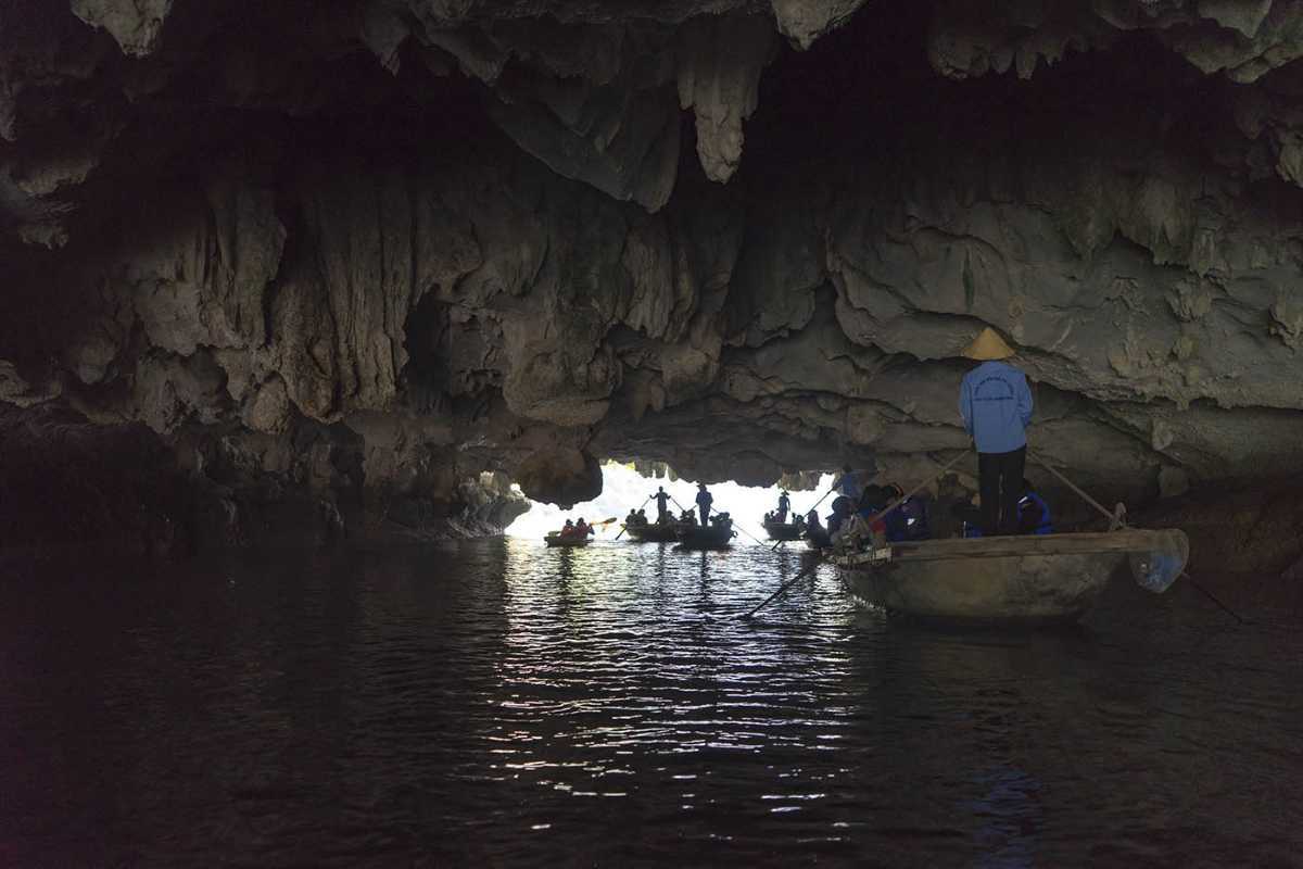 Dark and Bright Cave Halong Bay rowboats inside cavern Rowboats with visitors and guides traverse the dark interior of Dark and Bright Cave Halong Bay, heading toward daylight.