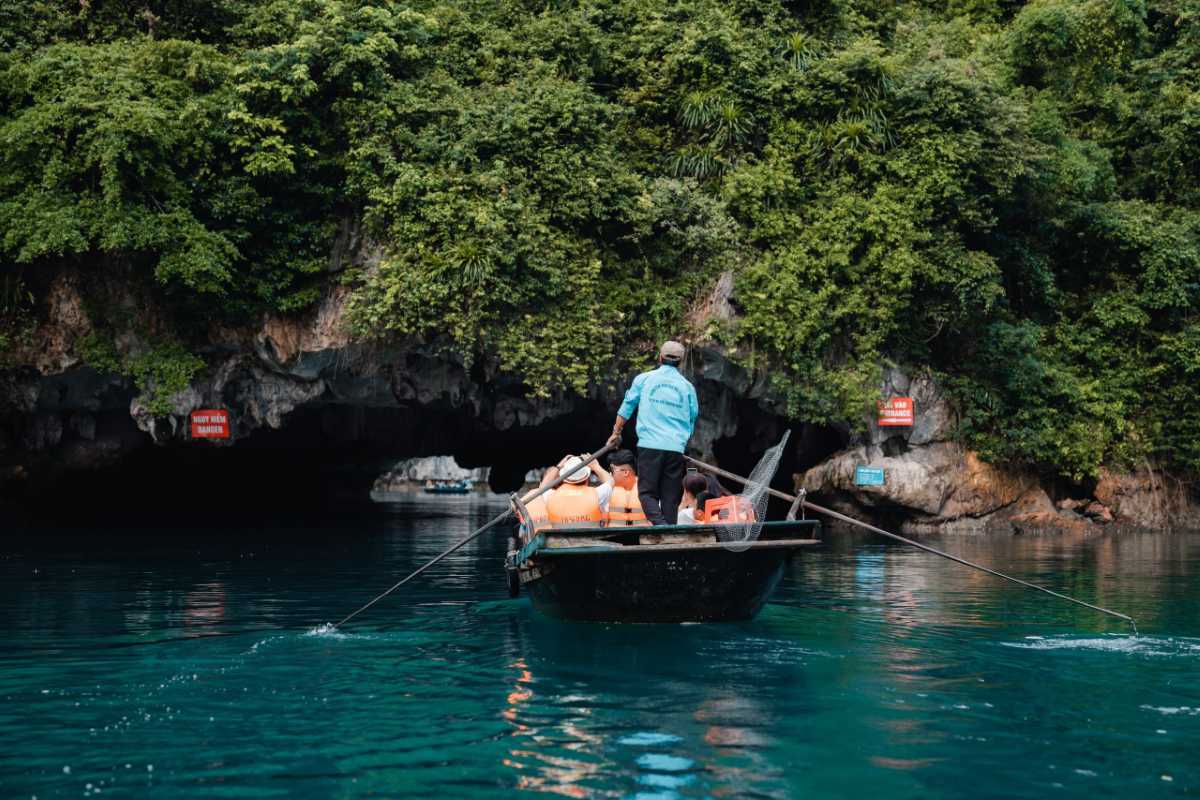 Dark and Bright Cave Halong Bay scenic boat approach Traditional bamboo boat approaching the entrance of Dark and Bright Cave Halong Bay, surrounded by dense jungle