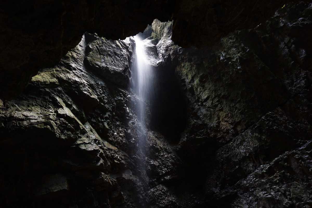 Dark and Bright Cave Halong Bay waterfall shaft Sunlight streaming through a shaft, illuminating a hidden waterfall inside Dark and Bright Cave Halong Bay