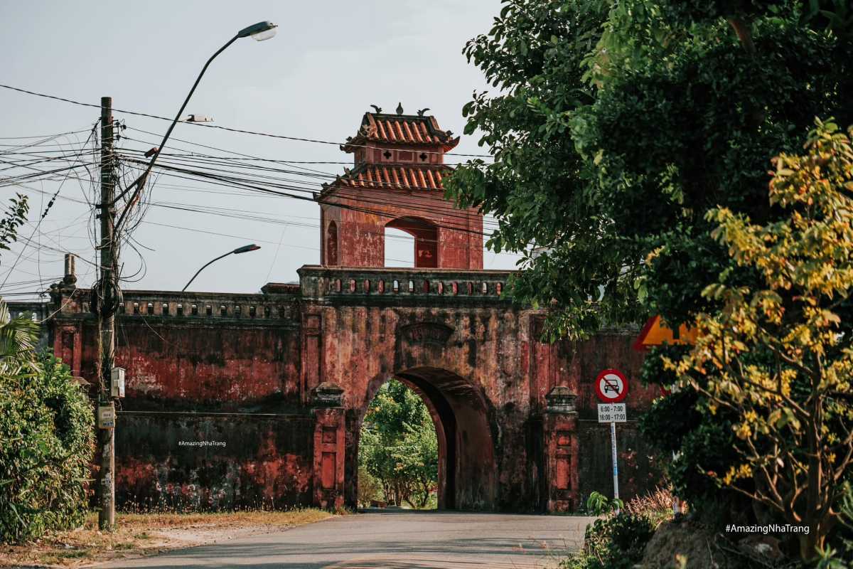 Side View of Dien Khanh Citadel Gate and Wall Side view of Dien Khanh Citadel’s red brick gate partly covered by trees and power lines.