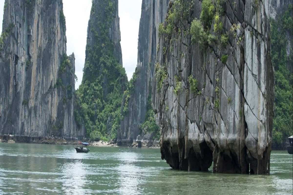 Dinh Huong Islet Halong Bay limestone cliffs with boats Limestone cliffs at Dinh Huong Islet Halong Bay with traditional boats sailing nearby