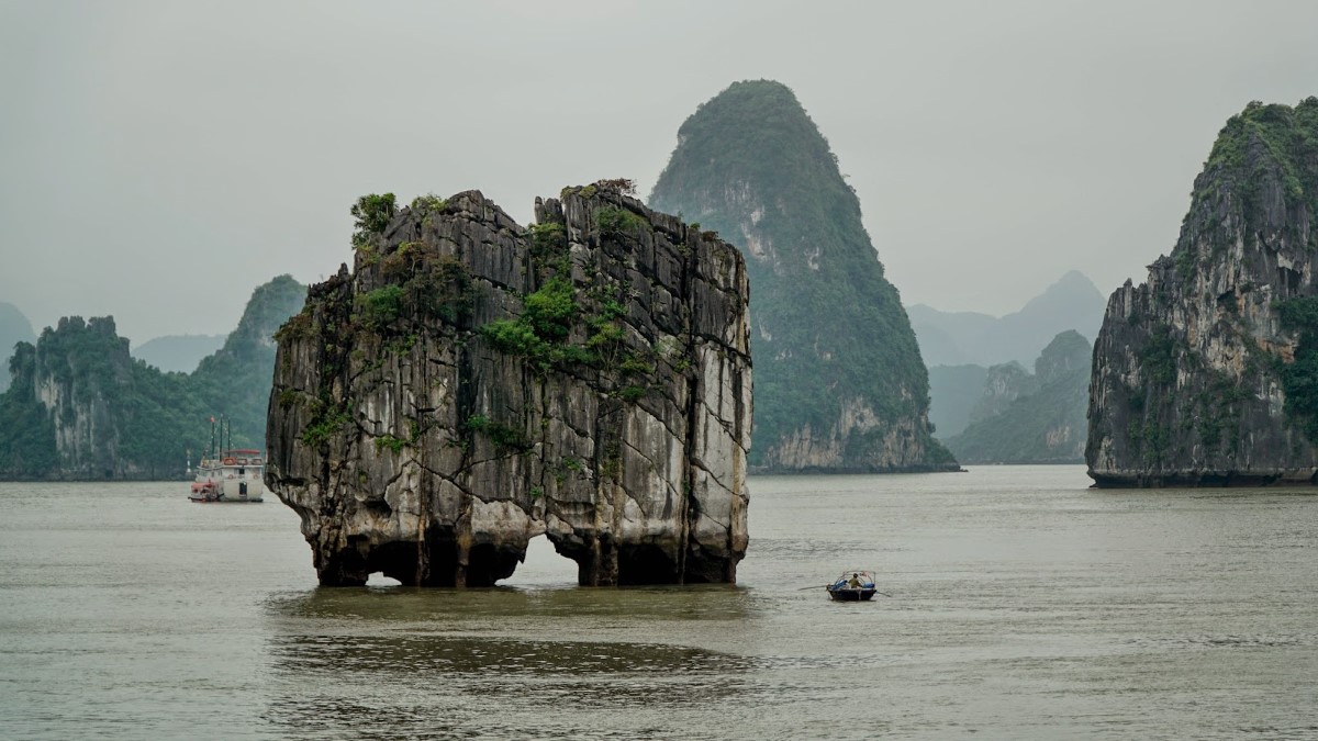 Dinh Huong Islet in Halong Bay, showing its unique rock formation surrounded by water and distant limestone mountains.