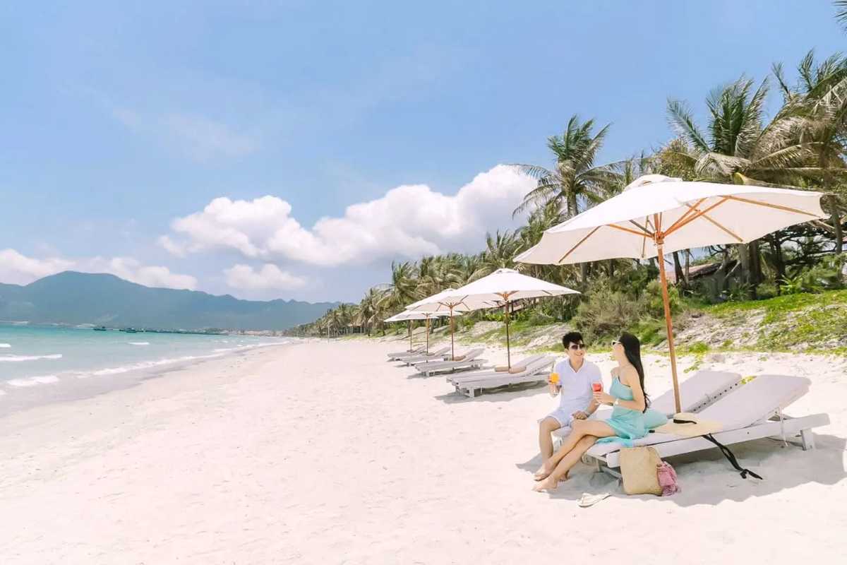 Couple Relaxing at Doc Let Beachfront Young couple seated under white umbrellas on soft sands of Doc Let Beach, enjoying tropical drinks with sea views.