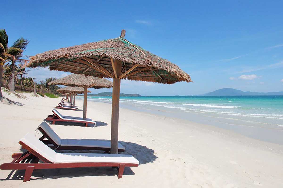 Empty Beach Loungers Facing Sea Empty loungers under straw huts line Doc Let Beach, with clear skies and waves gently touching the shore.