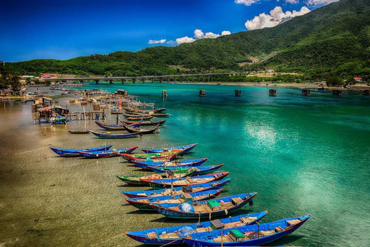 Docked Boats at Tranquil Fish Village Traditional Vietnamese boats anchored on clear shallow waters in front of a lush green backdrop near fish farms.
