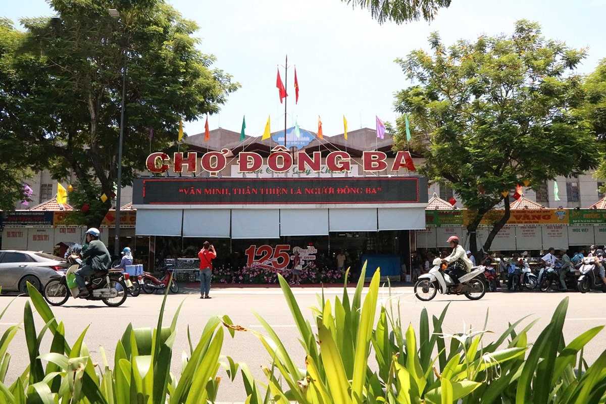 Main Entrance of Dong Ba Market Hue from Street View The main entrance of Dong Ba Market Hue seen from across the street, with flags, motorbikes, and greenery