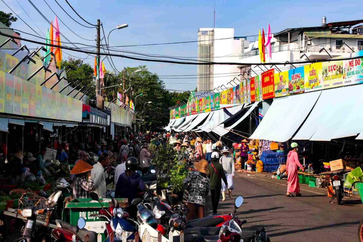 Morning Activity Outside Dong Ba Market Hue Morning scene outside Dong Ba Market in Hue with shoppers, scooters, and market stalls under bright flags