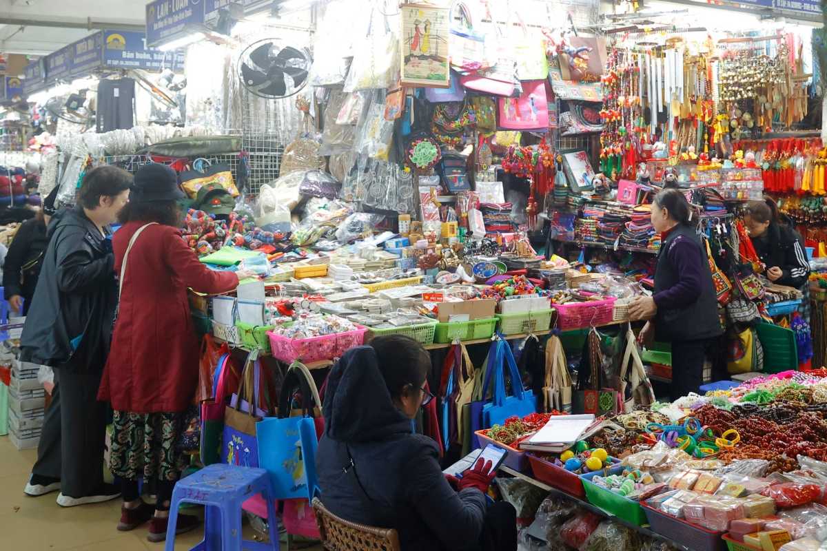 Busy Shopping Stalls with Bags and Accessories Shoppers browsing bags, backpacks, and accessories in Dong Xuan Market stalls.