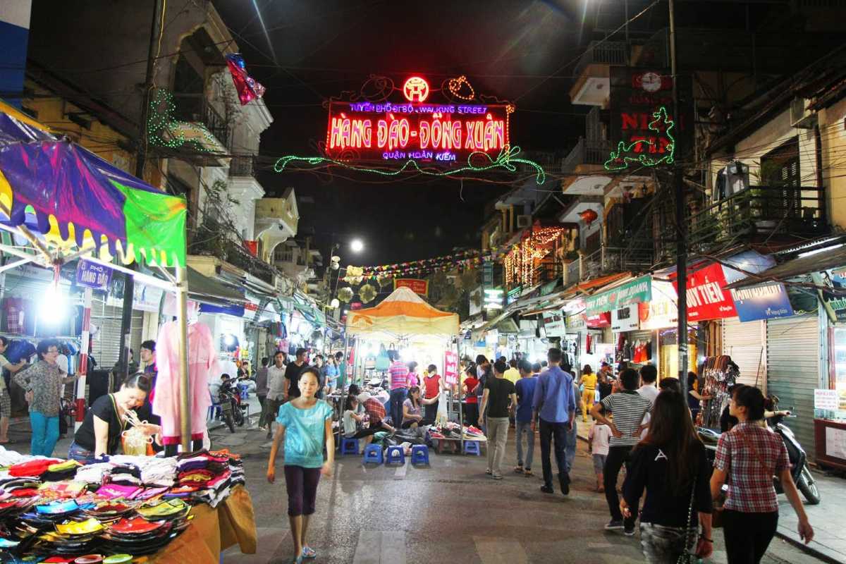 Tourists Shopping at Dong Xuan Market Hat Stalls Shoppers examining traditional hats and souvenirs at Dong Xuan Market stalls.