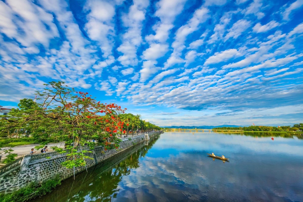 Scenic dragon boat ride on the Perfume River in Hue, Vietnam, surrounded by lush greenery and blue skies