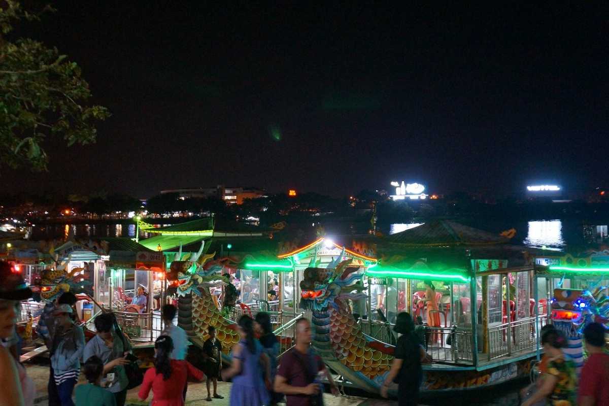 Dragon Boat Rides Along Perfume River Near Walking Street Dragon boats docked along the Perfume River at night with visitors enjoying the riverside near Nguyen Dinh Chieu Street