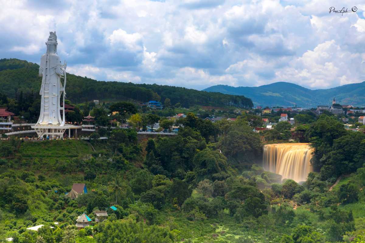 Elephant Waterfall Da Lat statue Quan Am nearby View of Elephant Waterfall Da Lat with the large white Quan Am statue and temple on a hill nearby under blue skies