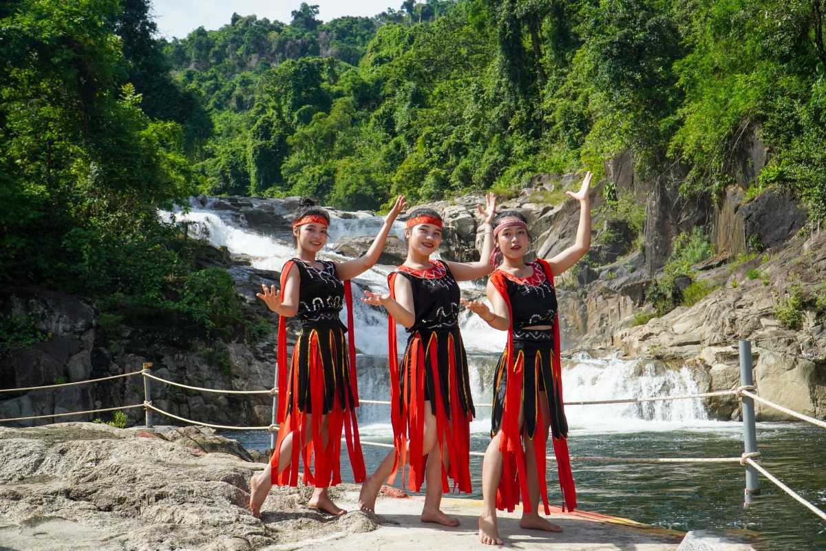 Ethnic dance performance by Cai River Three women in red-and-black ethnic costumes performing a cultural dance near a river waterfall in Nha Trang.