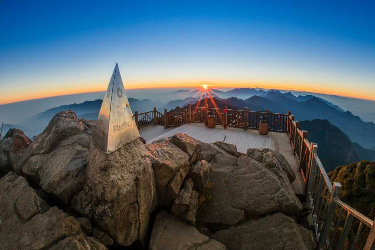 Fansipan Mountain Sapa summit marker sunrise panoramic view Fansipan Mountain Sapa summit marker at sunrise, golden sun over distant mountains, expansive wooden deck