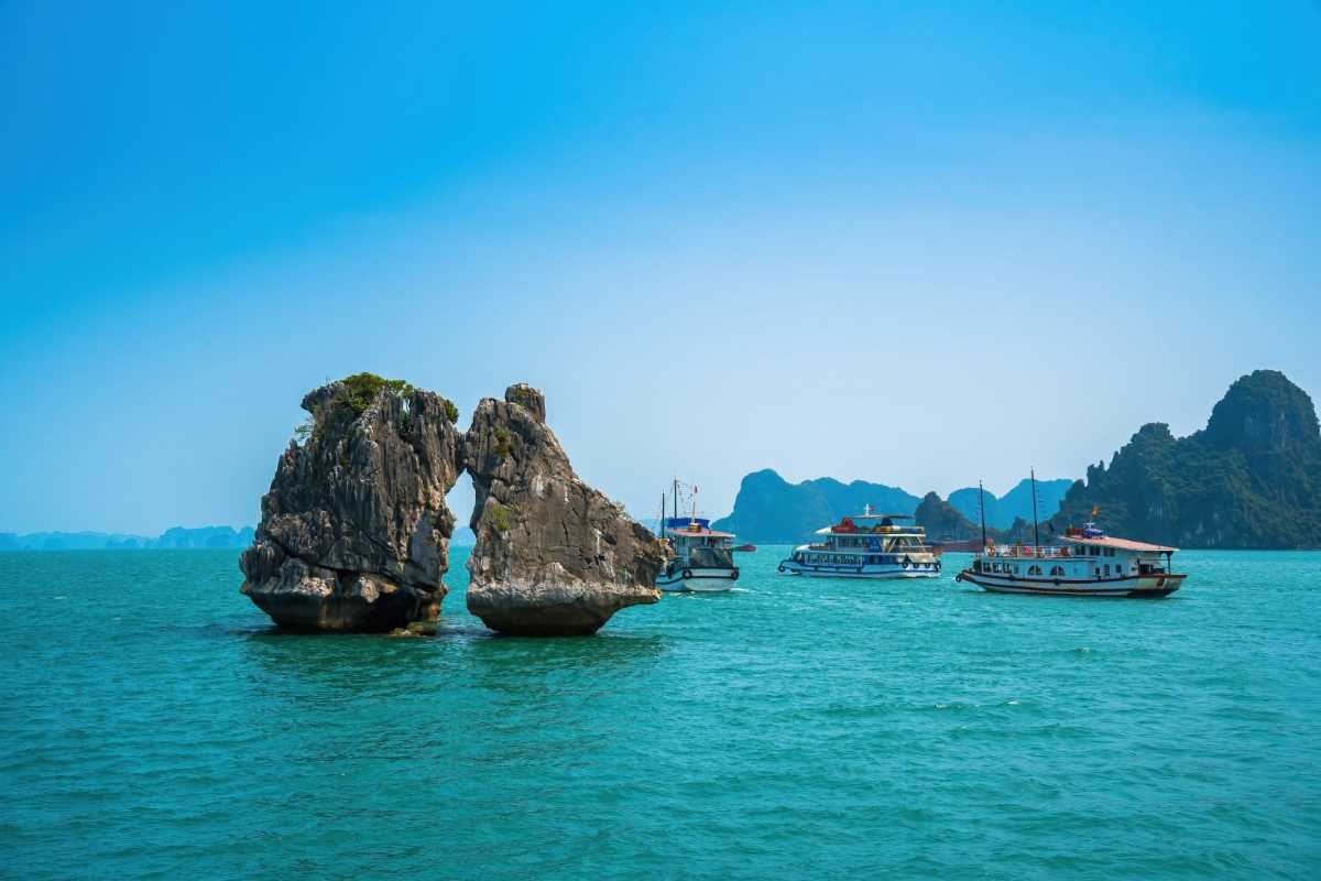 Fighting Cocks Islet Halong Bay Close-up with Boats Nearby Close-up of Fighting Cocks Islet Halong Bay limestone rocks with nearby tourist boats sailing in calm waters.