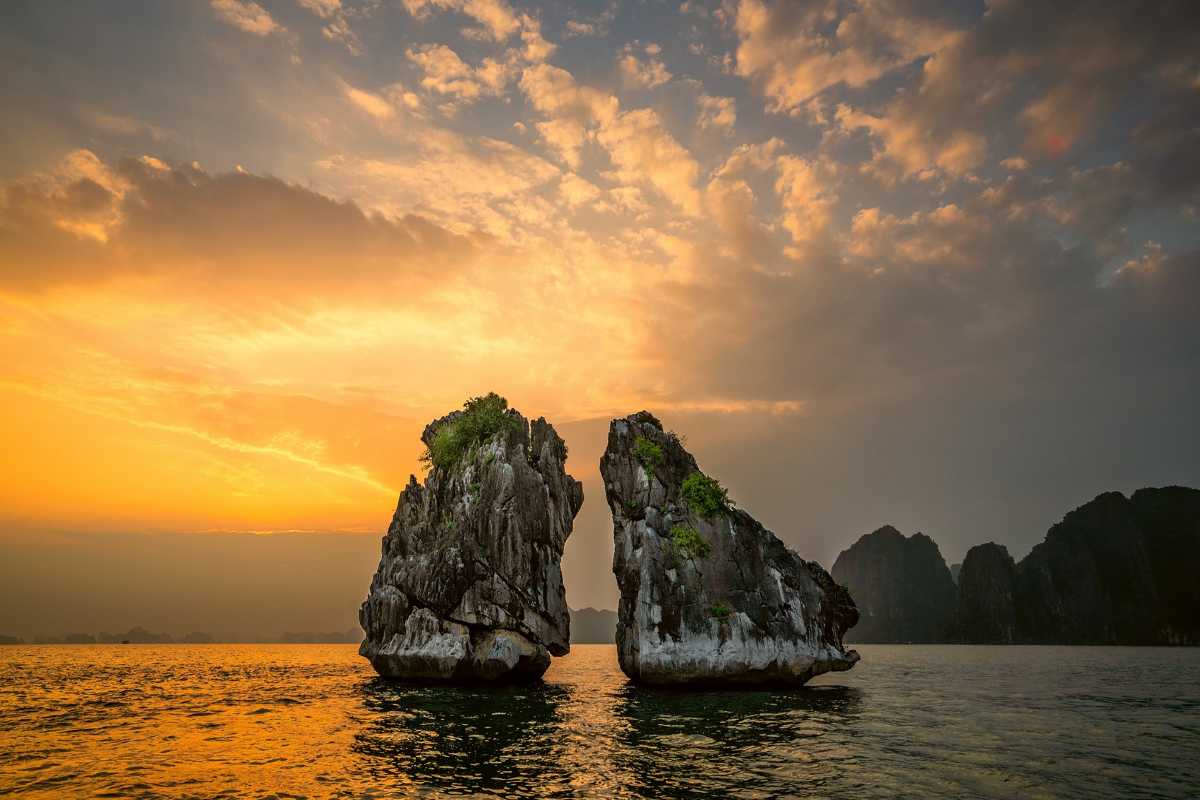 Fighting Cocks Islet Halong Bay sunset glow Fighting Cocks Islet Halong Bay at sunset with golden sky reflecting on calm waters