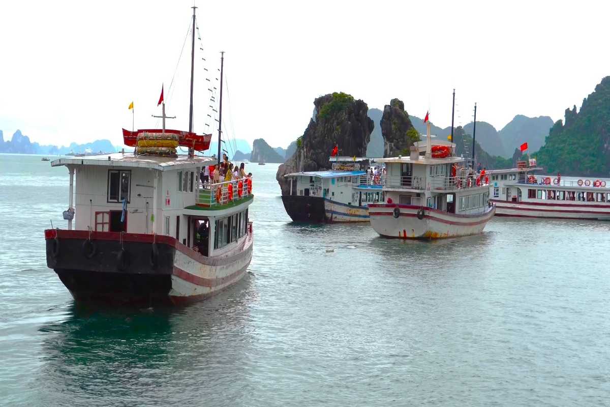 Fighting Cocks Islet Halong Bay tour boat near rocks Traditional tour boat cruising close to Fighting Cocks Islet Halong Bay limestone rocks