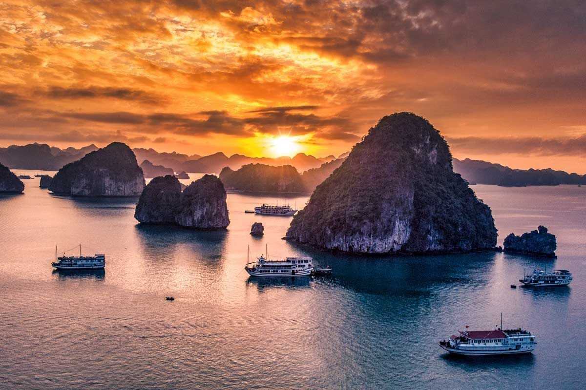 Fighting Cocks Islet Halong Bay with Traditional Boats in Daylight Traditional Vietnamese boats sailing near Fighting Cocks Islet Halong Bay on a bright, clear day.