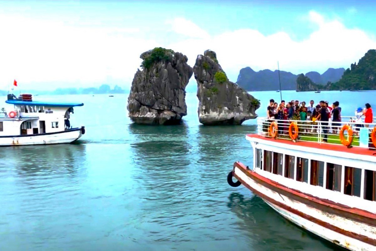 A view of Fighting Cocks Islet in Halong Bay with two tour boats nearby. The famous rock formation appears in the middle of the bay.