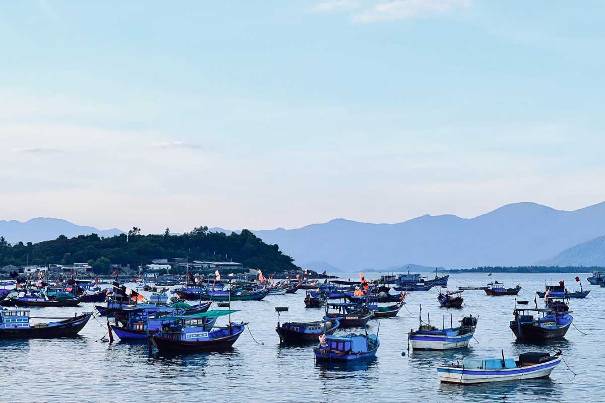 Colorful fishing boats docked in calm waters at Vĩnh Lương, with mountain silhouettes in the background.