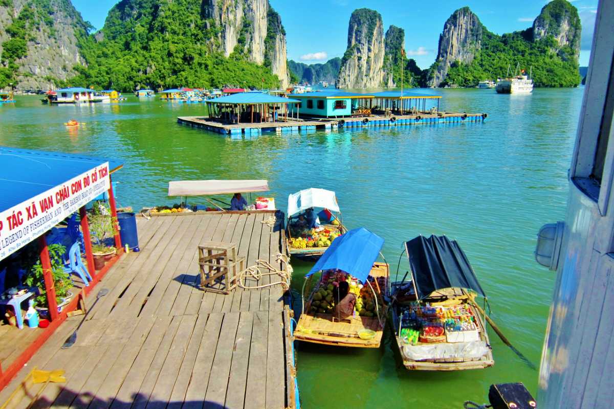 Floating Shops and Bamboo Boats in Ba Hang Floating fruit and snack boats dock near wooden piers in Ba Hang Fishing Village with karsts in the background.